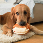 A calm Golden Retriever dog lying on a light rug, gently holding the plush strawberry croissant dog toy in its mouth, demonstrating a comforting and relaxed interaction with the soft fabric.